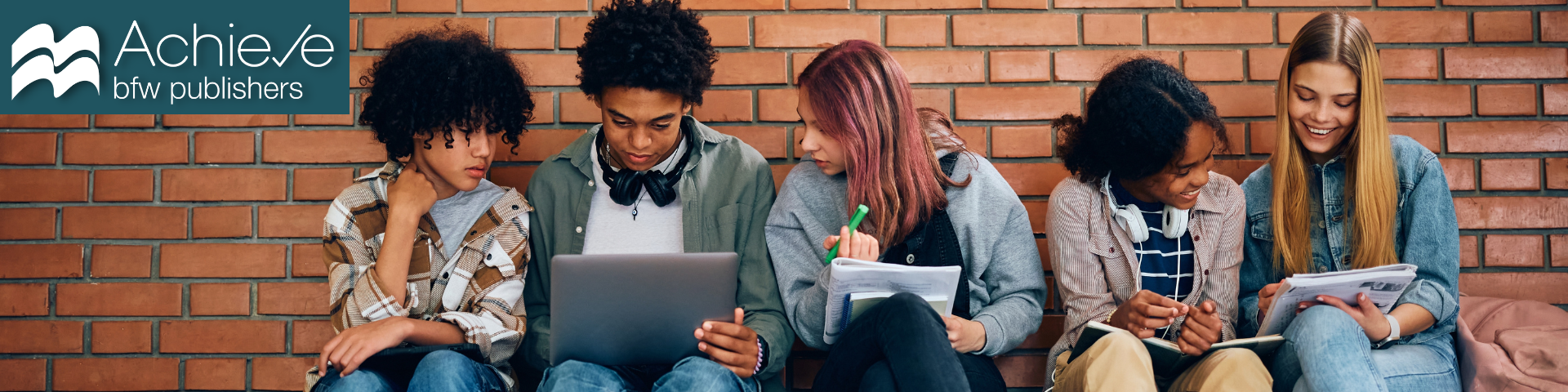 photograph of five students doing homework together against a brick wall.