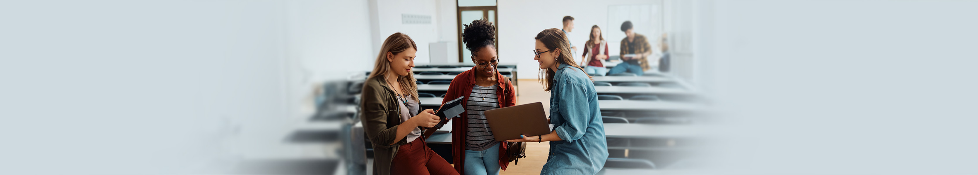 Multiracial group of female students using wireless technology in university classroom.